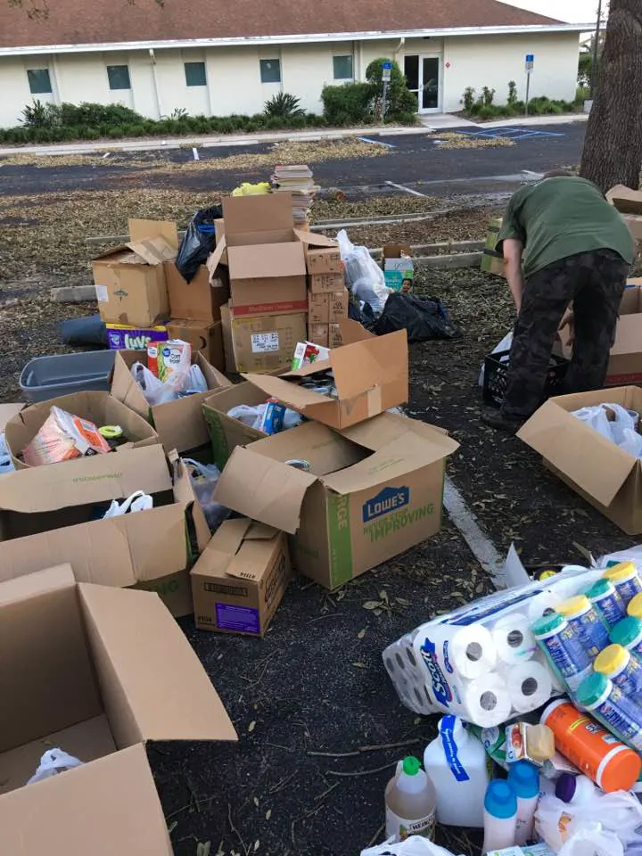Open boxes of donated goods, paper towels and cleaning supplies spread across a parking lot while a volunteer sorts them.